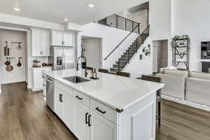 Kitchen featuring a kitchen bar, white cabinets, open floor plan, stainless steel appliances, and a center island with sink