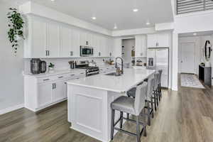 Kitchen featuring white cabinets, stainless steel appliances, a kitchen island with sink, a kitchen breakfast bar, and dark wood-type flooring