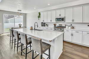 Kitchen featuring a kitchen island with sink, white cabinets, a kitchen bar, stainless steel appliances, and a textured ceiling
