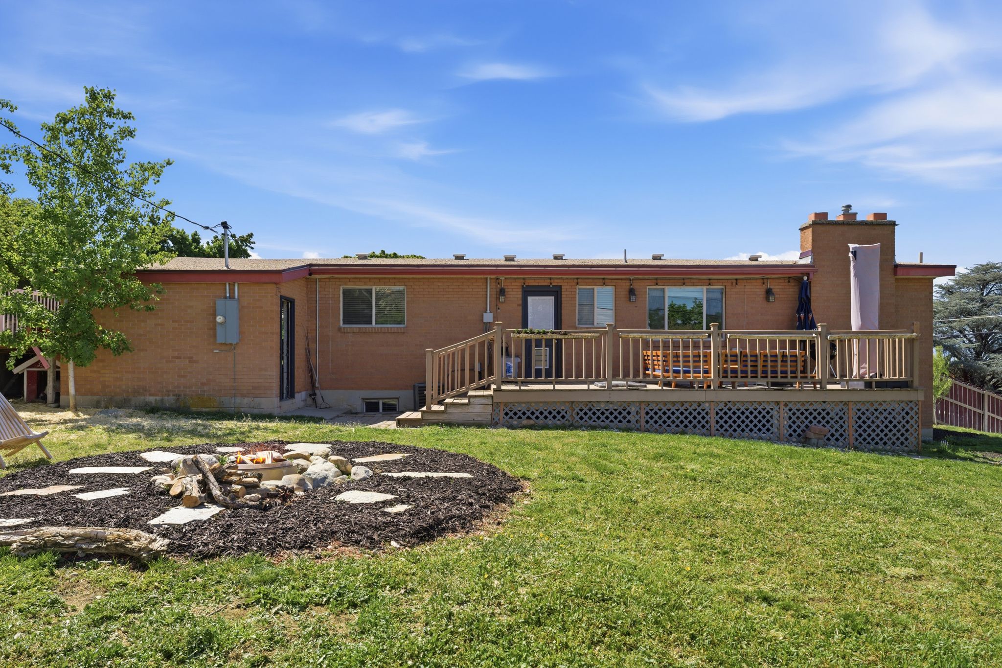 Back of house with a deck, brick siding, a chimney, a fire pit, and a yard