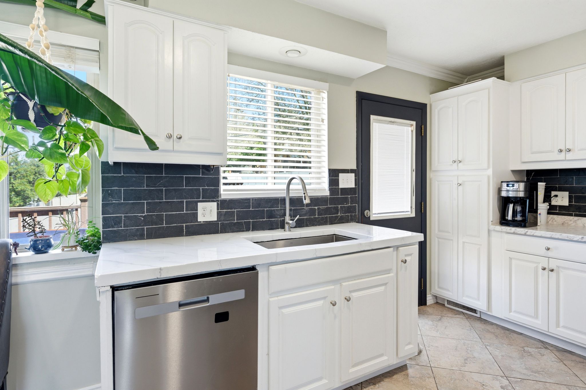 Kitchen with light stone countertops, stainless steel dishwasher, white cabinets, decorative backsplash, and crown molding