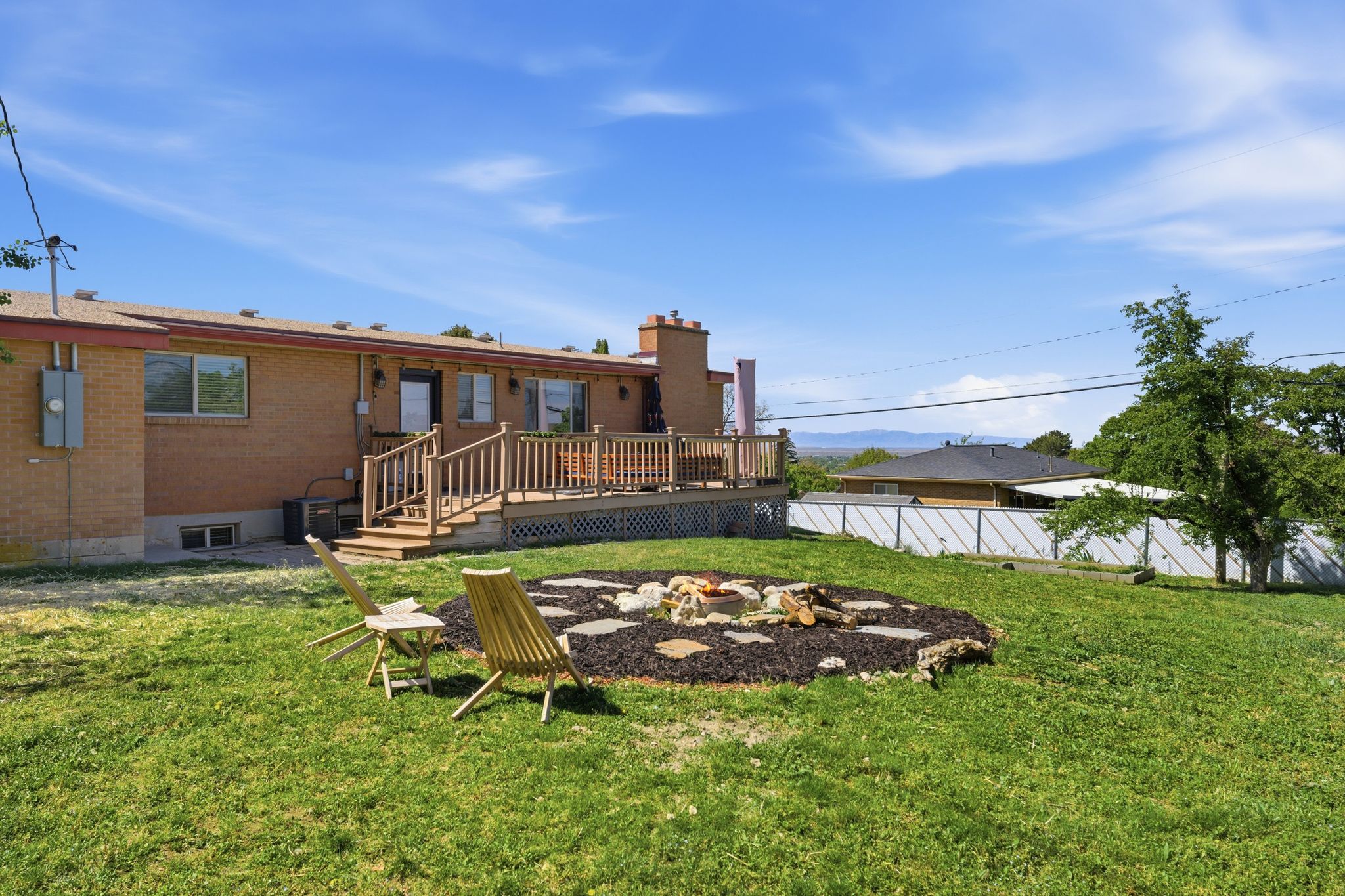 Back of house featuring a fire pit, a deck, a chimney, and brick siding