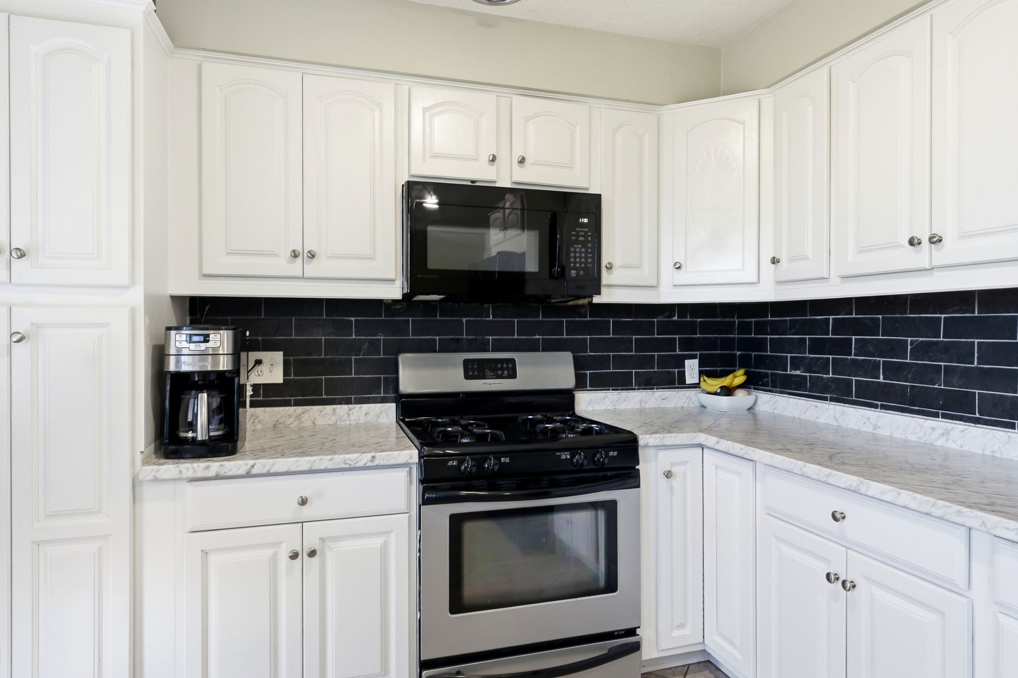 Kitchen with stainless steel gas range, white cabinetry, black microwave, and tasteful backsplash