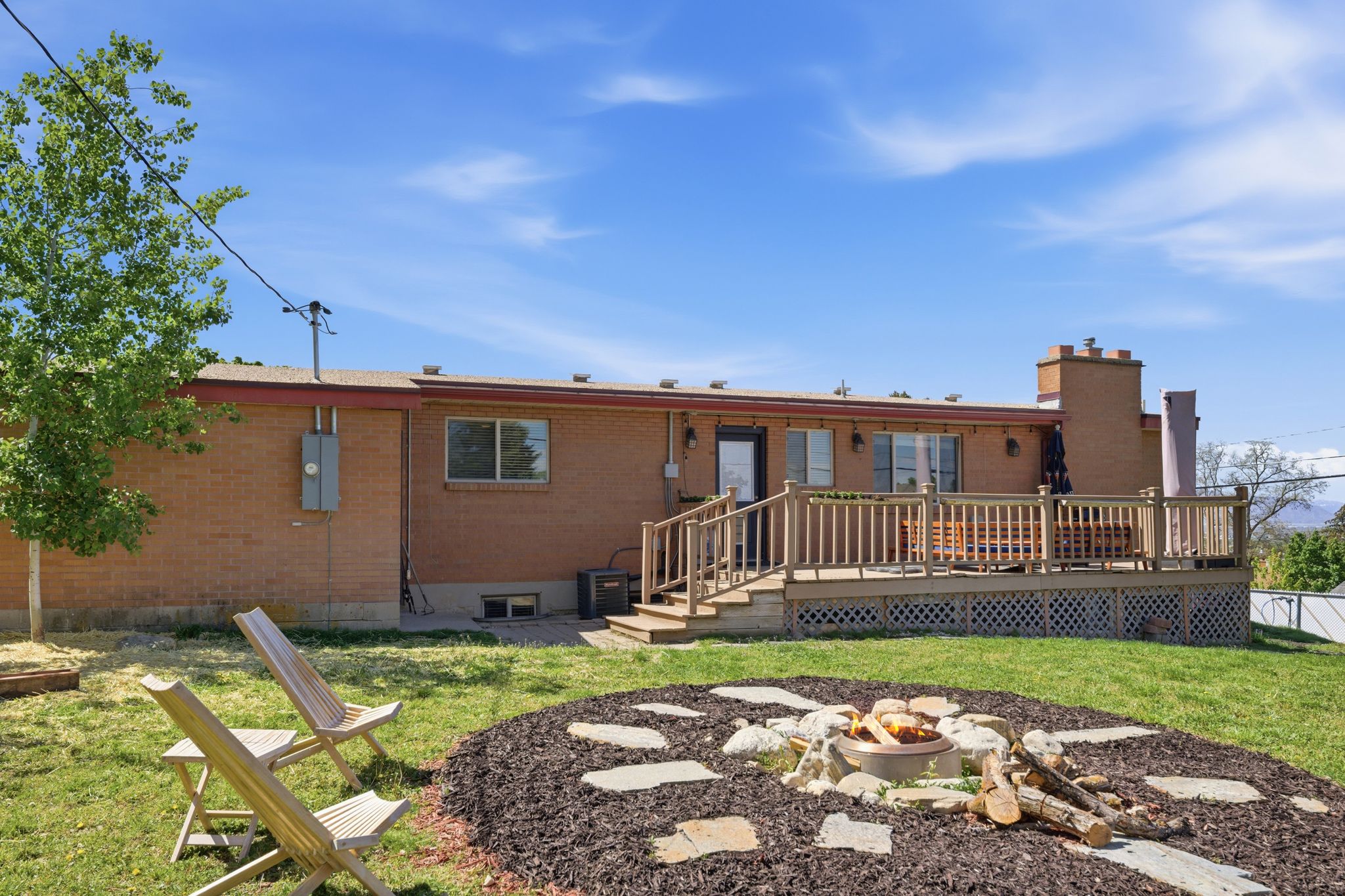 Back of house with brick siding, a deck, a fire pit, a lawn, and a chimney