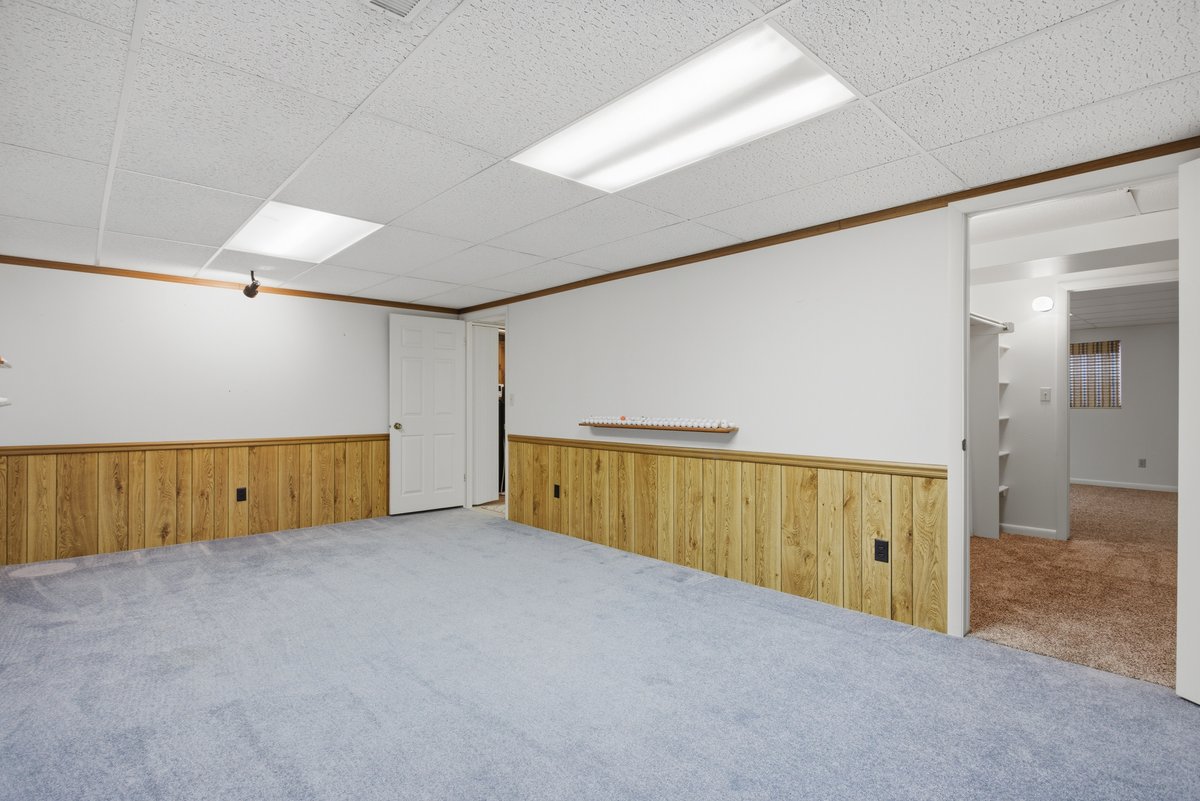 Carpeted empty room featuring wood walls, ornamental molding, a drop ceiling, and a wainscoted wall
