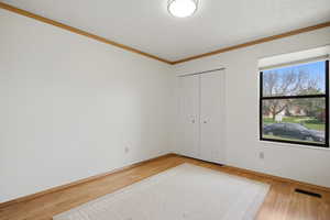 Unfurnished bedroom with light wood finished floors, a closet, and crown molding
