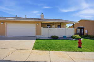 Ranch-style home featuring an attached garage, brick siding, concrete driveway, a gate, and a chimney