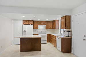 Kitchen with light flooring, light countertops, wood finish cabinets, white appliances, and a kitchen island