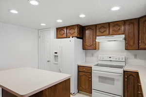Kitchen with white appliances, light countertops, wallpapered walls, recessed lighting, and a kitchen island