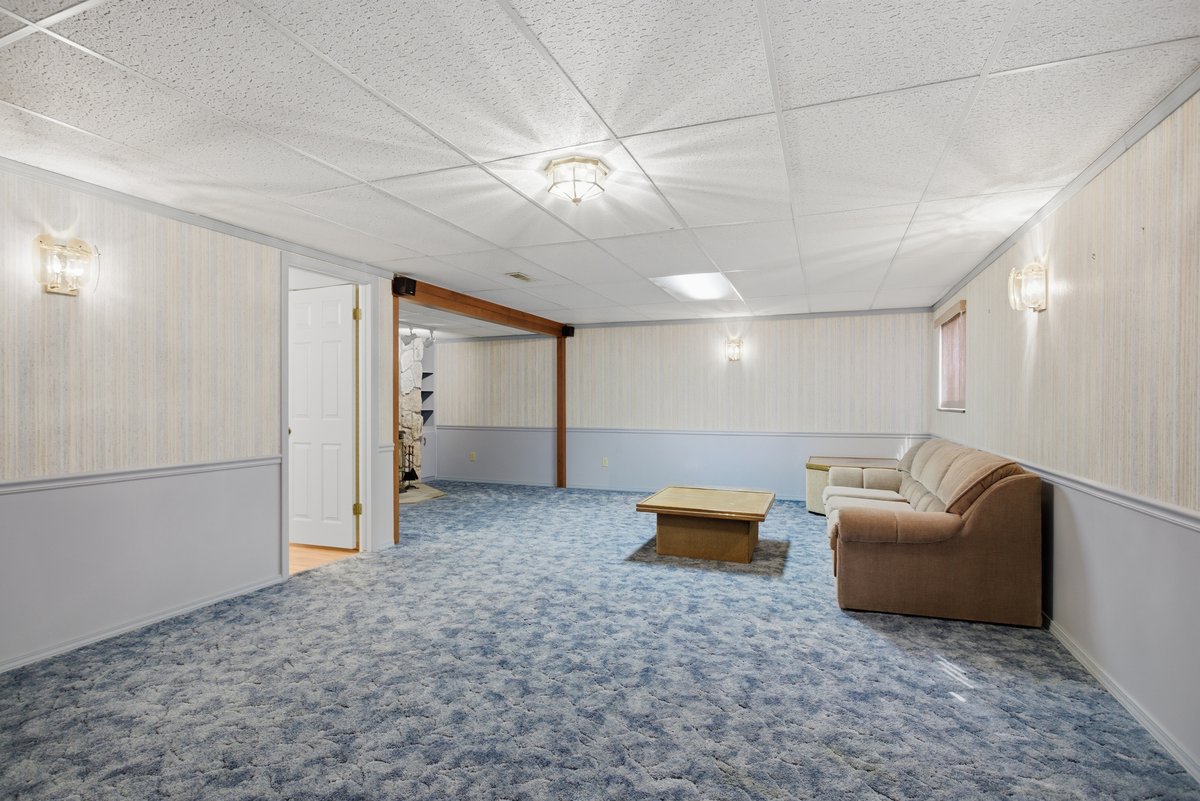 Living area with a paneled ceiling, a wainscoted wall, carpet flooring, and wood walls