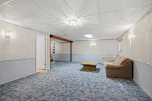 Living area with a paneled ceiling, a wainscoted wall, carpet flooring, and wood walls
