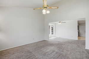 Carpeted spare room featuring ceiling fan and vaulted ceiling
