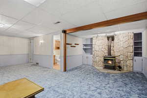 Finished below grade area with a drop ceiling, a wood stove, carpet, and built in features