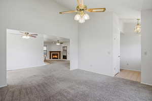 Unfurnished living room with a fireplace with flush hearth, light carpet, a ceiling fan, and lofted ceiling