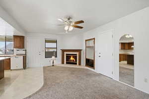 Unfurnished living room featuring ceiling fan, a fireplace, light carpet, arched walkways, and a textured ceiling