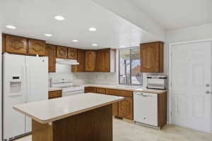 Kitchen featuring light floors, white appliances, light countertops, wood finish cabinetry, and a kitchen island