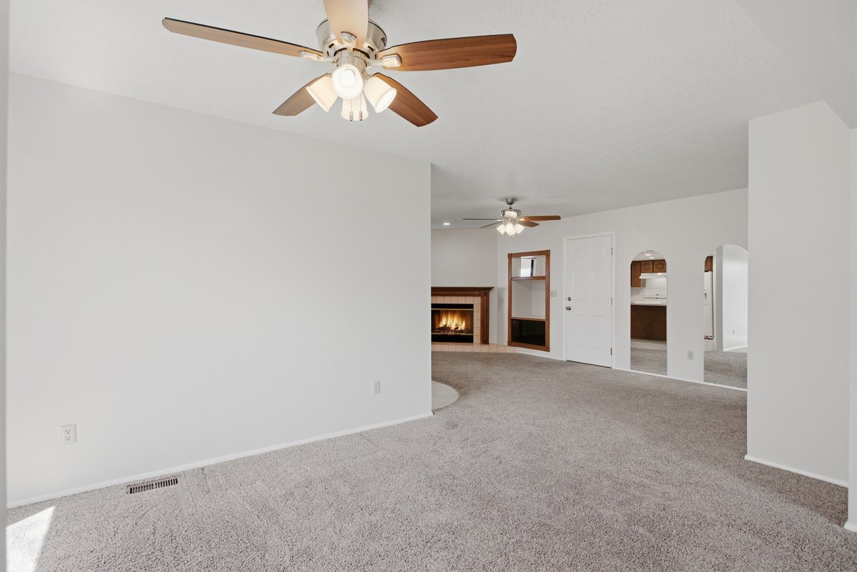 Unfurnished living room with a lit fireplace, carpet flooring, arched walkways, and a ceiling fan