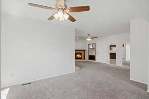 Unfurnished living room with a lit fireplace, carpet flooring, arched walkways, and a ceiling fan