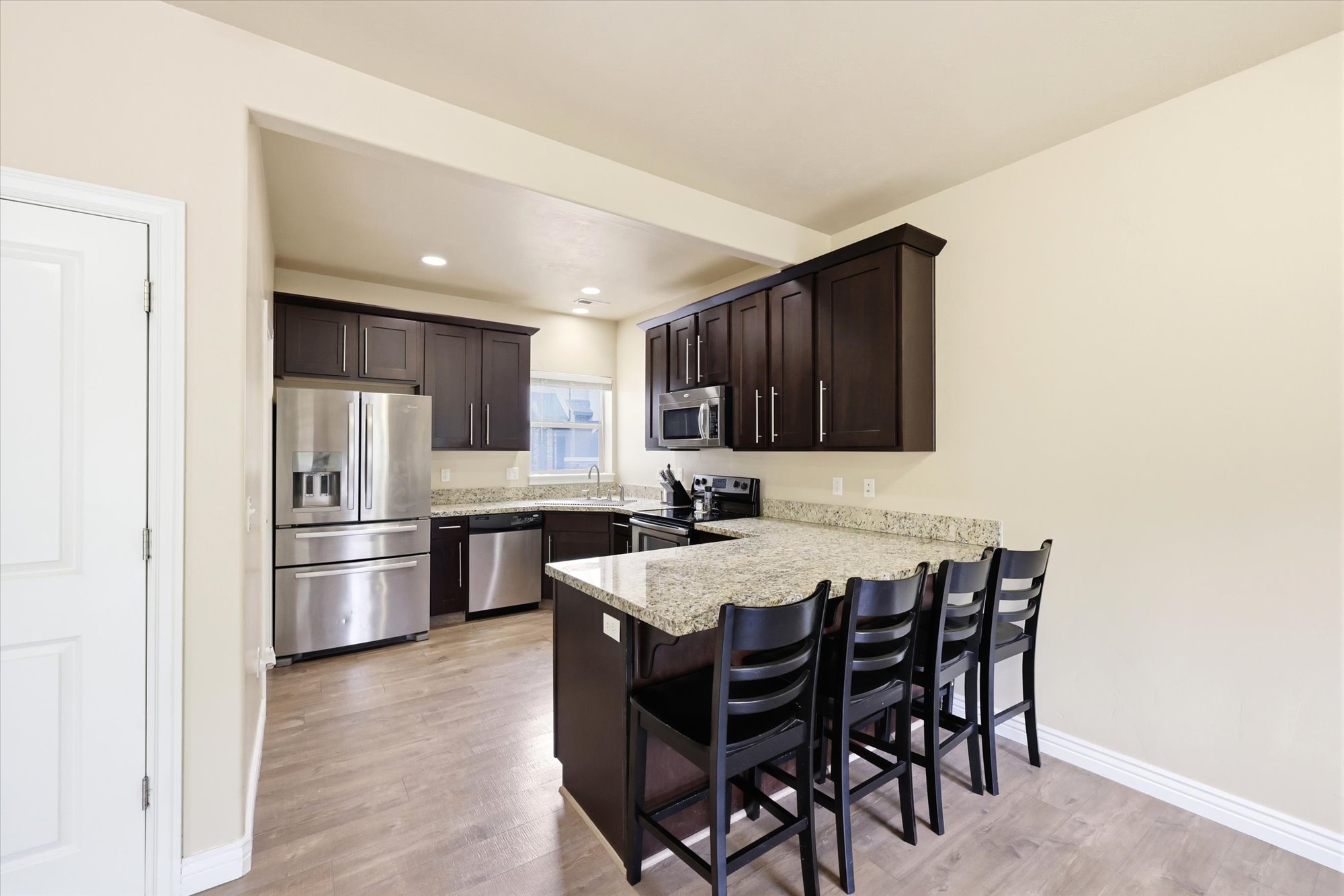 Kitchen with dark wood finish cabinetry, stainless steel appliances, a kitchen bar, a peninsula, and recessed lighting