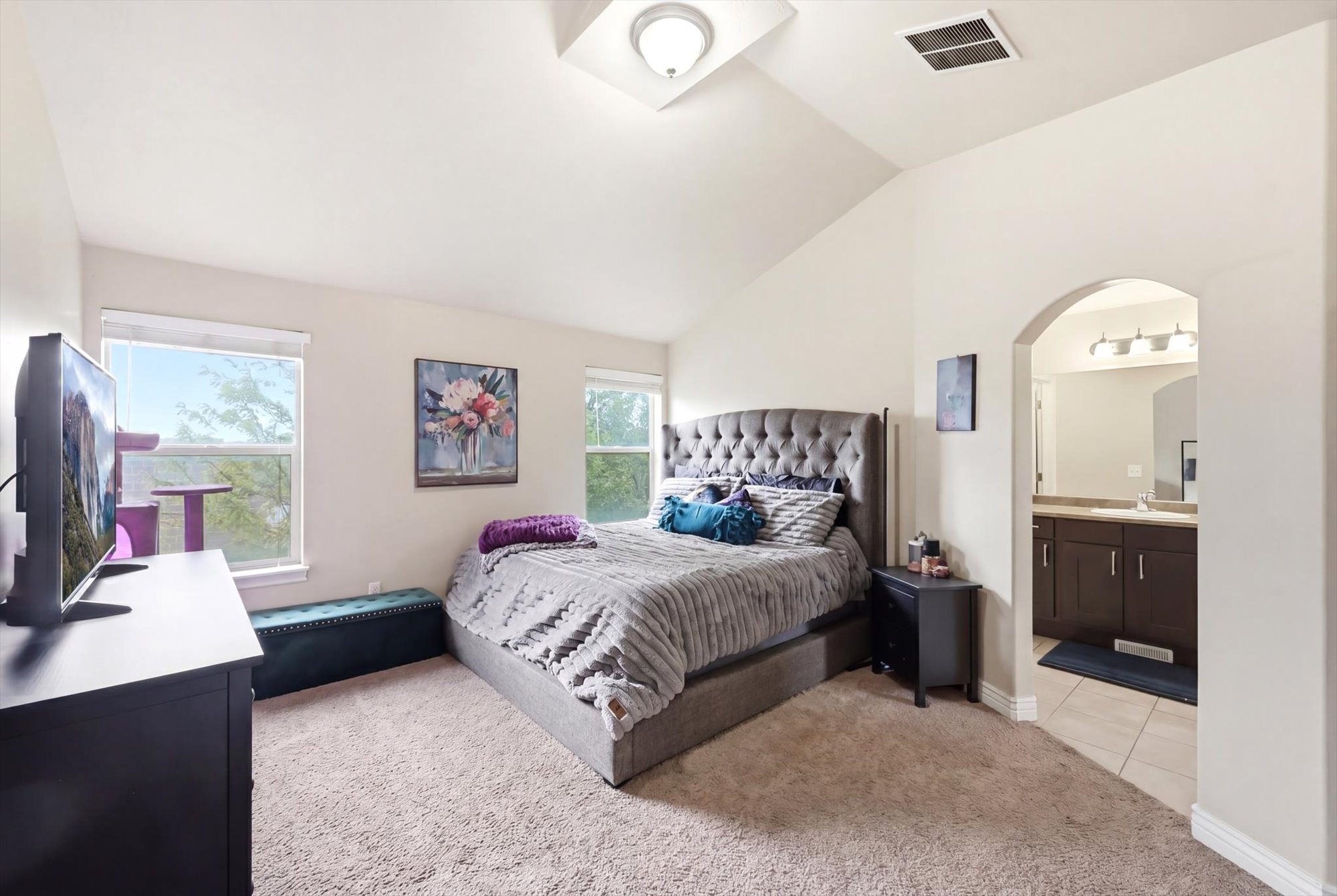 Primary Bedroom featuring light colored carpet, vaulted ceiling, and ensuite bath