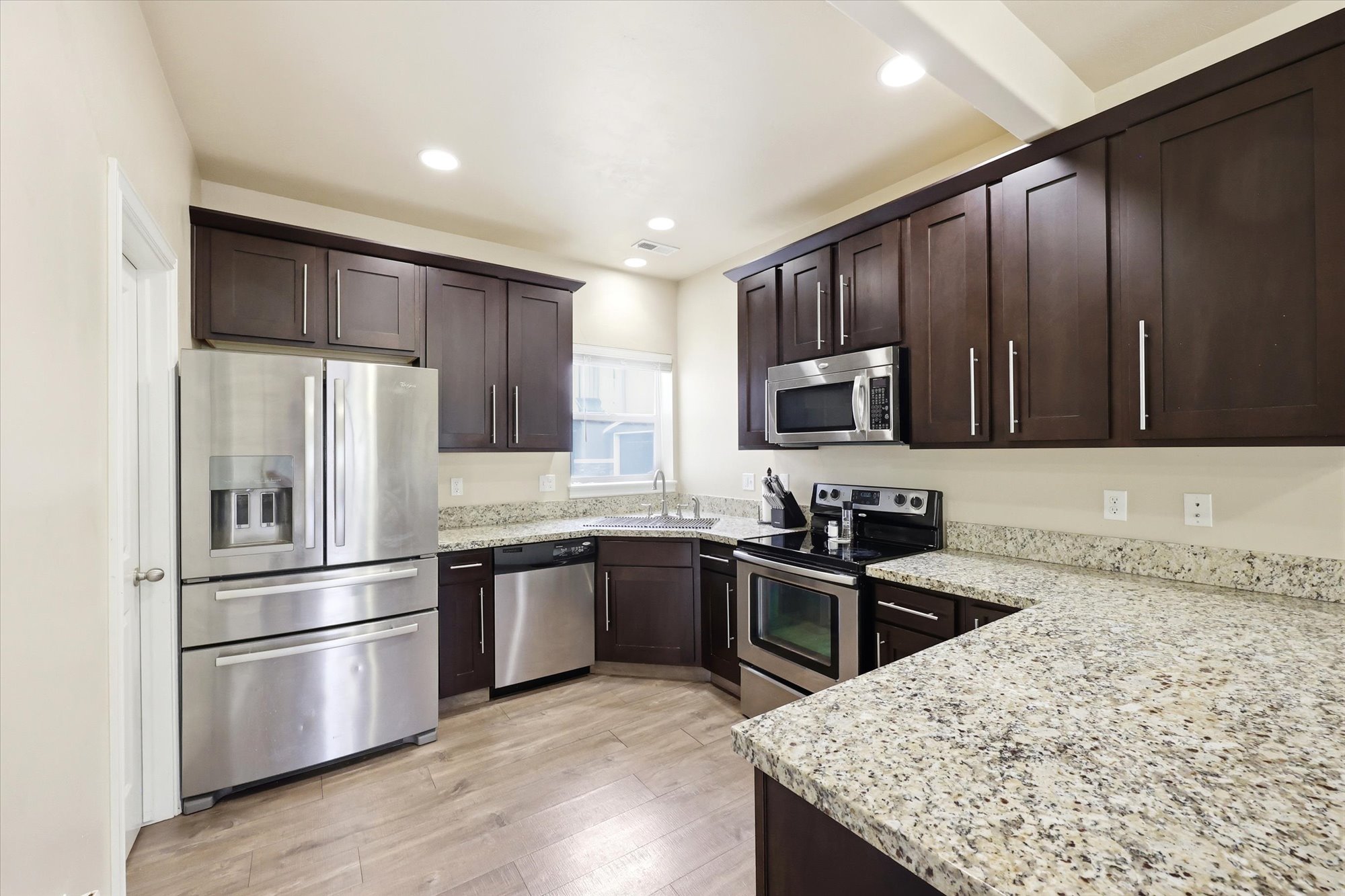 Kitchen featuring stainless steel appliances, dark wood finish cabinetry, light stone counters, light wood finished floors, and recessed lighting