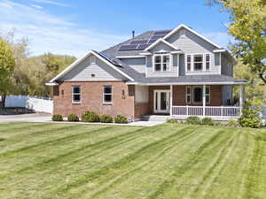 View of front of house featuring roof mounted solar panels, a porch, brick siding, and a shingled roof