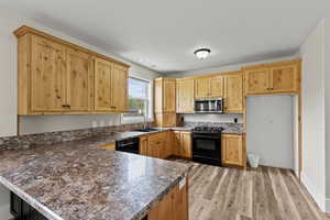 Kitchen featuring black appliances, a peninsula, light wood finished floors, and light wood finish cabinetry