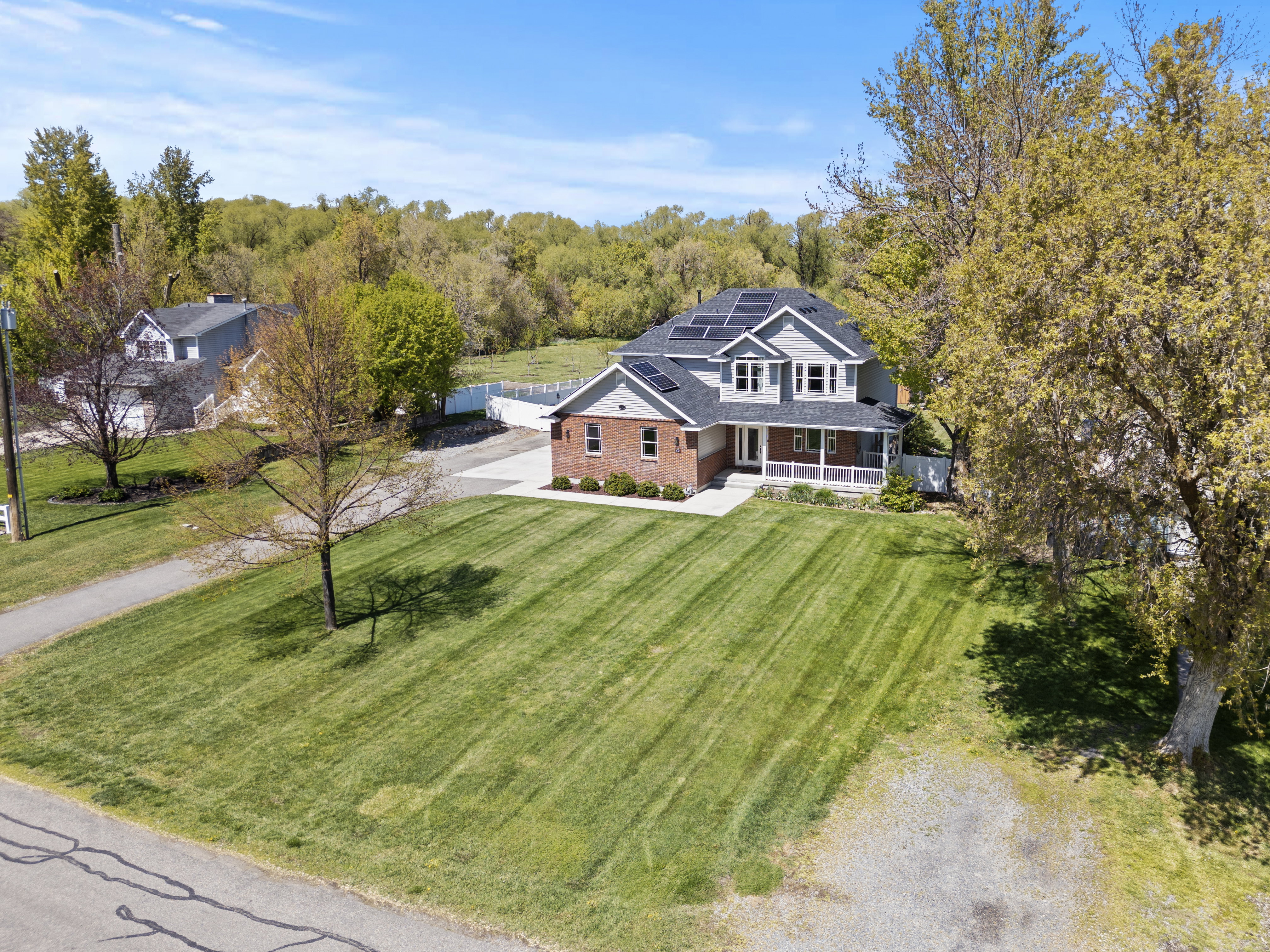 View of front of house featuring covered porch, solar panels, driveway, a front yard, and brick siding