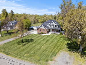 View of front of house featuring covered porch, solar panels, driveway, a front yard, and brick siding