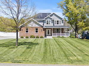 View of front of house with a porch, roof mounted solar panels, brick siding, and a shingled roof