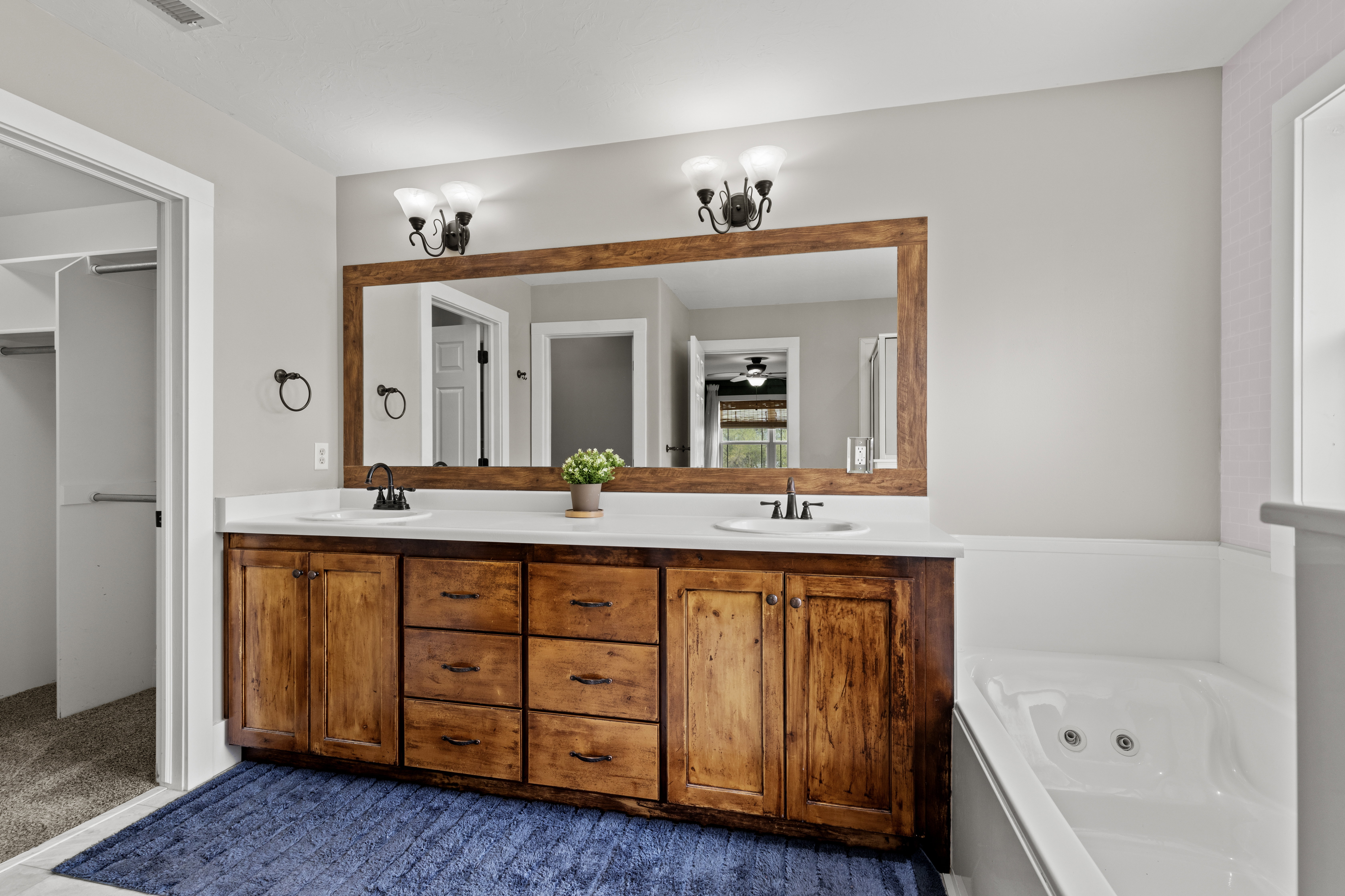 Bathroom with double vanity, a jetted tub, a spacious closet, and dark colored carpet