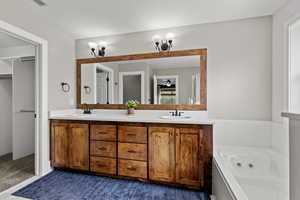 Bathroom with double vanity, a jetted tub, a spacious closet, and dark colored carpet