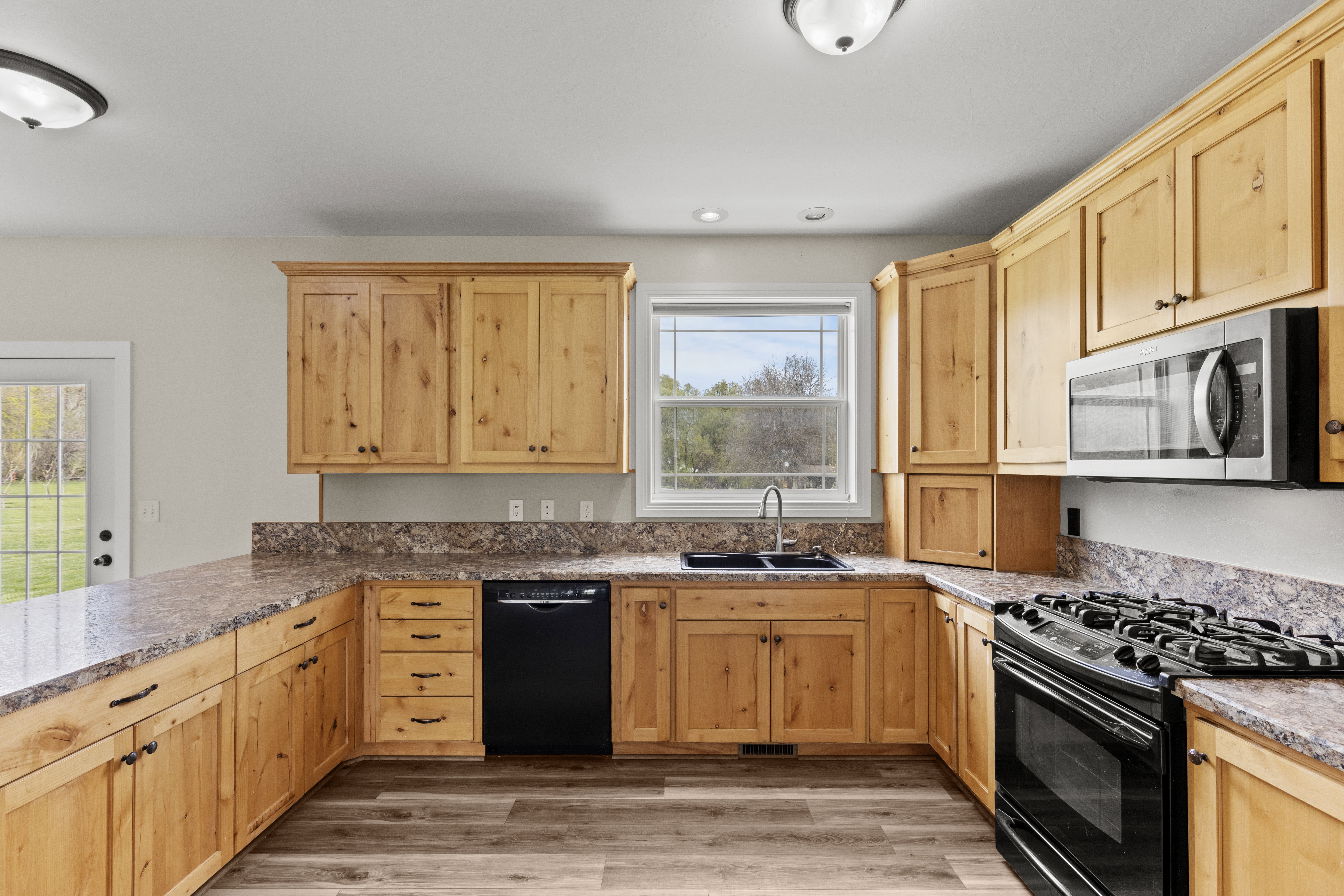 Kitchen featuring light wood finish cabinets, black appliances, light wood-style flooring, a peninsula, and recessed lighting
