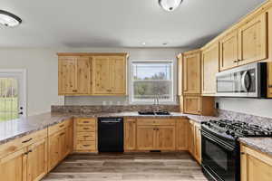 Kitchen featuring light wood finish cabinets, black appliances, light wood-style flooring, a peninsula, and recessed lighting