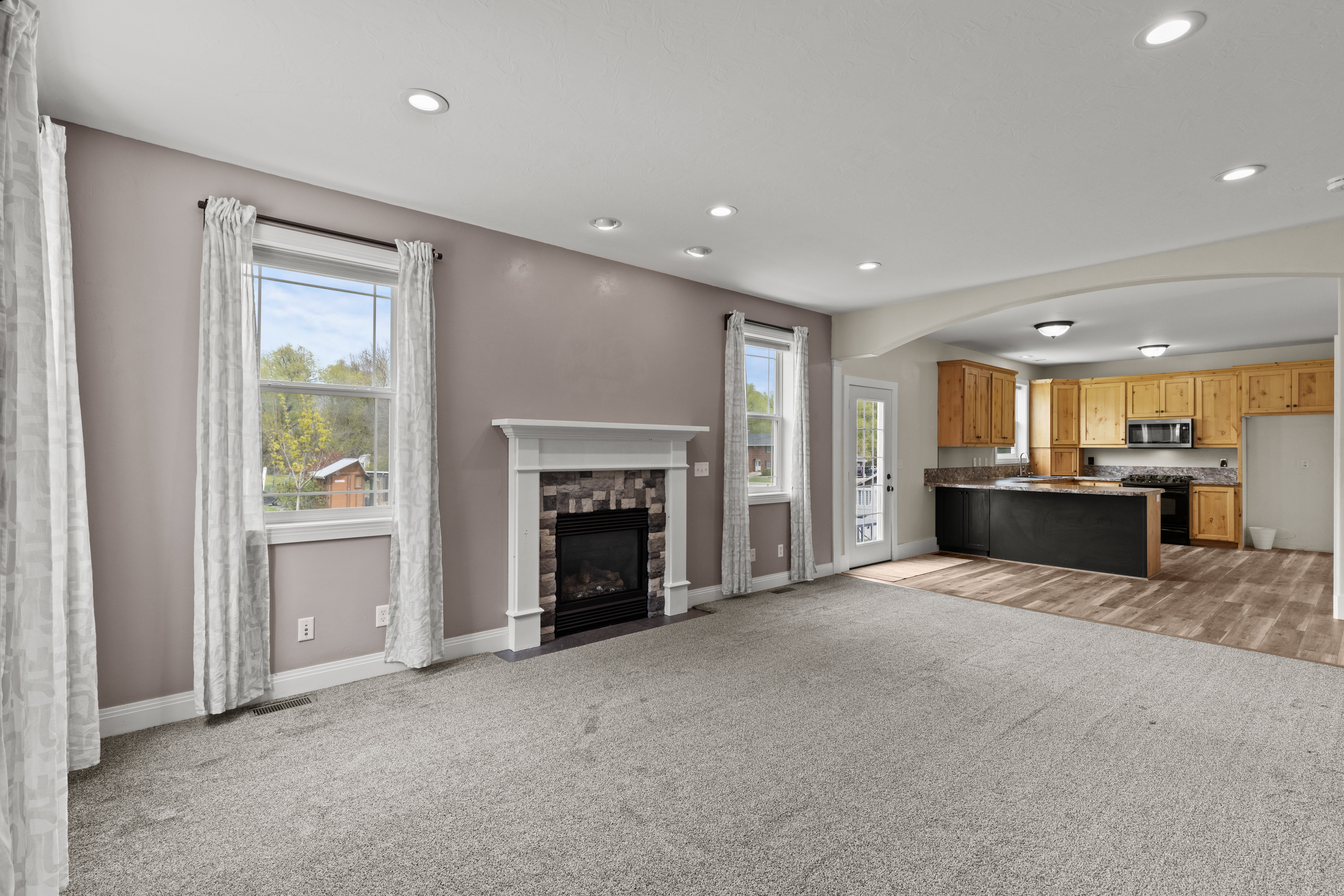 Unfurnished living room with arched walkways, light colored carpet, a fireplace, and recessed lighting