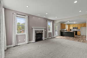Unfurnished living room with arched walkways, light colored carpet, a fireplace, and recessed lighting