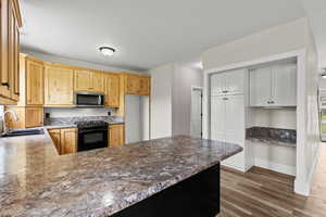 Kitchen featuring black range oven, stainless steel microwave, dark wood-style floors, light wood finish cabinetry, and a peninsula