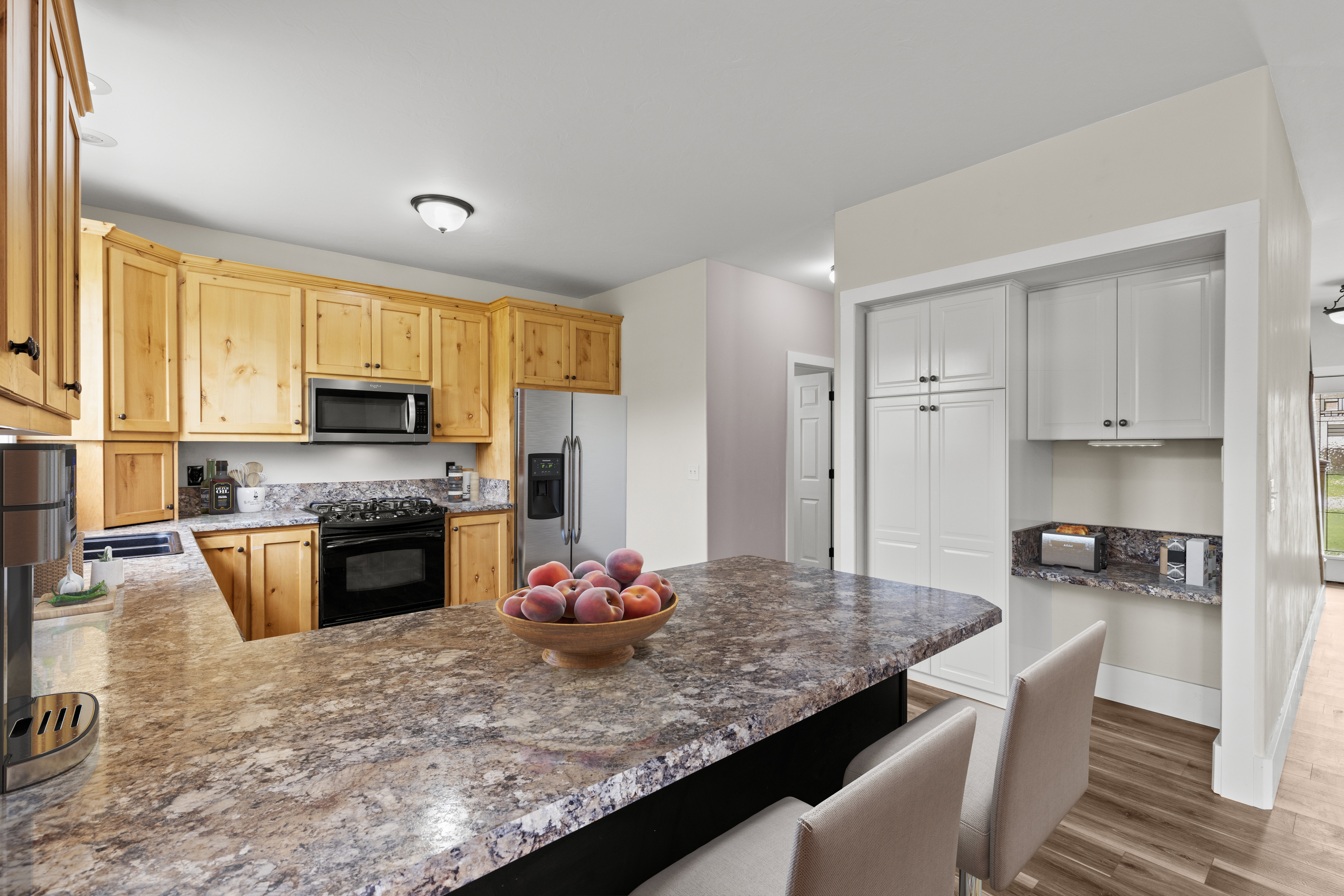 Kitchen with stainless steel appliances, a peninsula, dark wood-style floors, light wood finish cabinetry, and a breakfast bar area