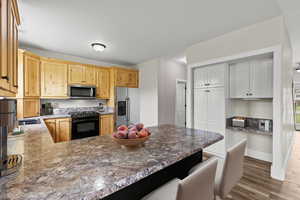 Kitchen with stainless steel appliances, a peninsula, dark wood-style floors, light wood finish cabinetry, and a breakfast bar area