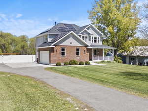 Traditional-style home with solar panels, brick siding, a porch, driveway, and a shingled roof