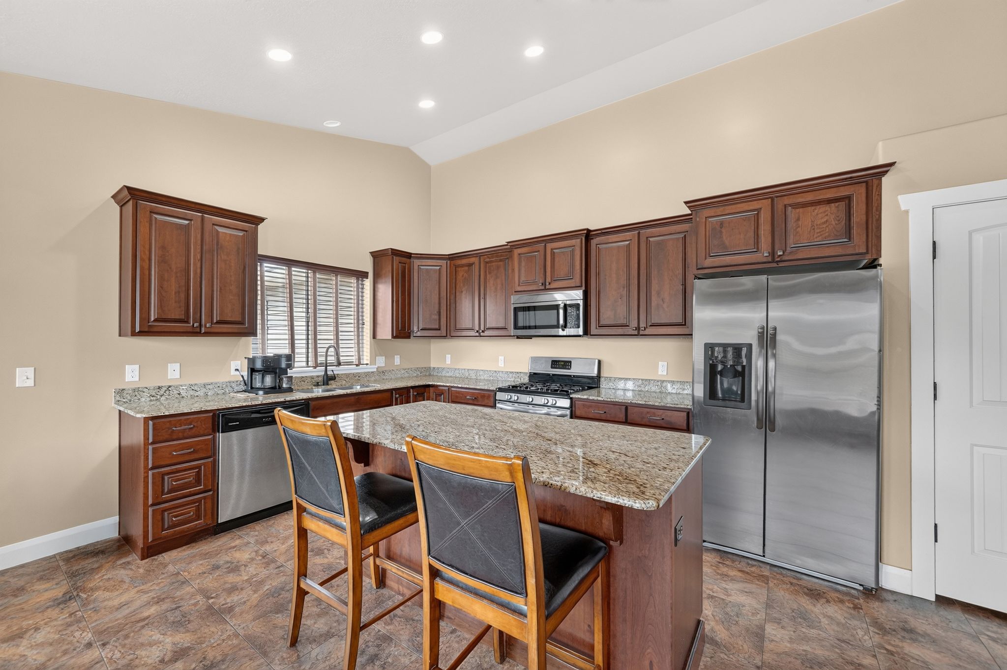 Kitchen featuring an L-shaped layout with dark wood cabinetry, granite countertops, and stainless steel appliances