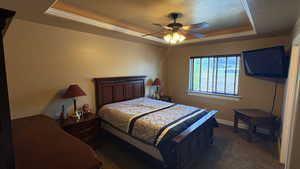 Master Bedroom with a tray ceiling, a ceiling fan, dark colored carpet, and a textured ceiling