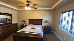 Master Bedroom with a raised ceiling, dark colored carpet, crown molding, and a ceiling fan