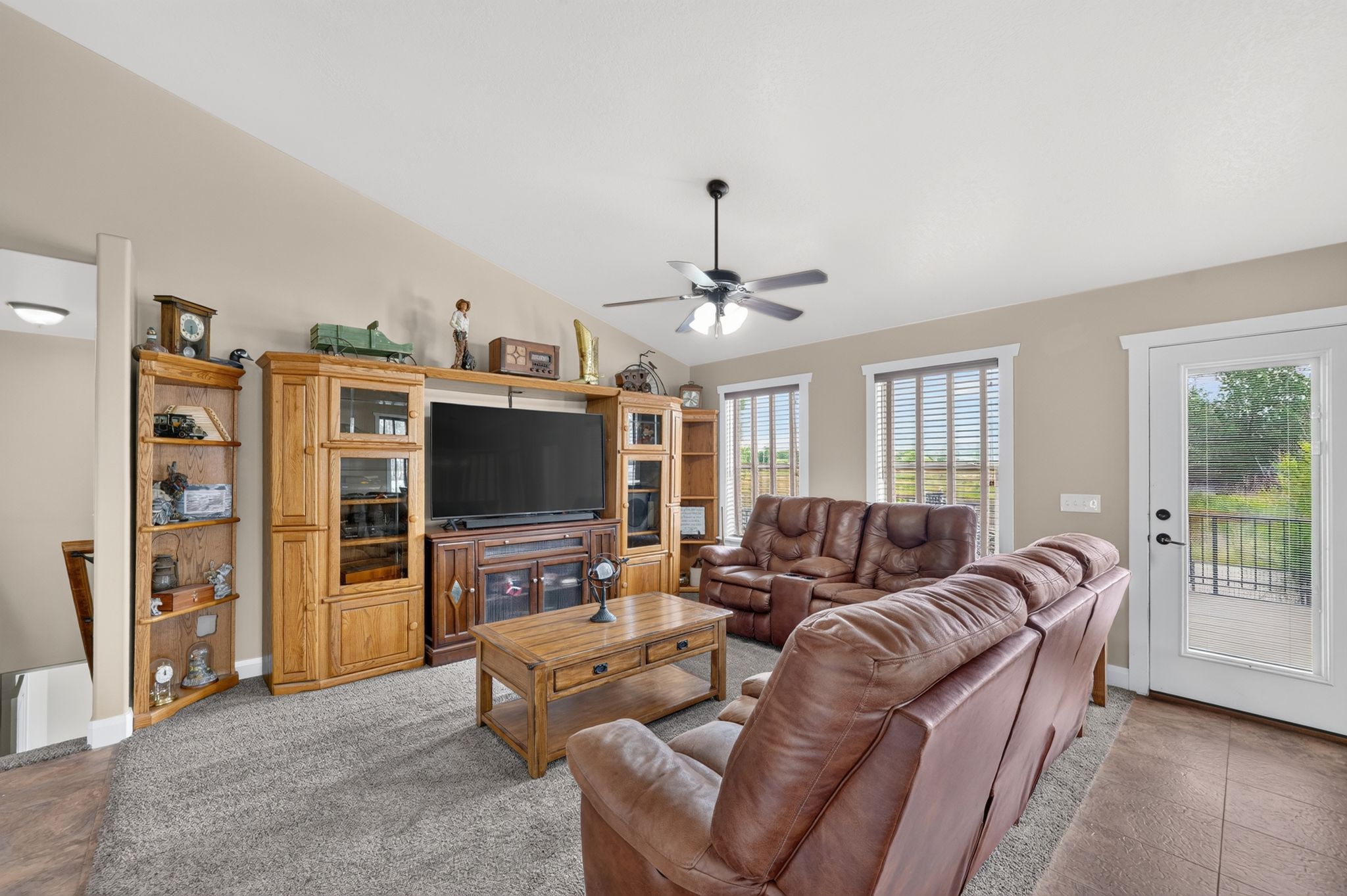 Living area featuring a vaulted ceiling with a ceiling fan, carpet flooring, and a glass-paned door opening onto an outdoor deck
