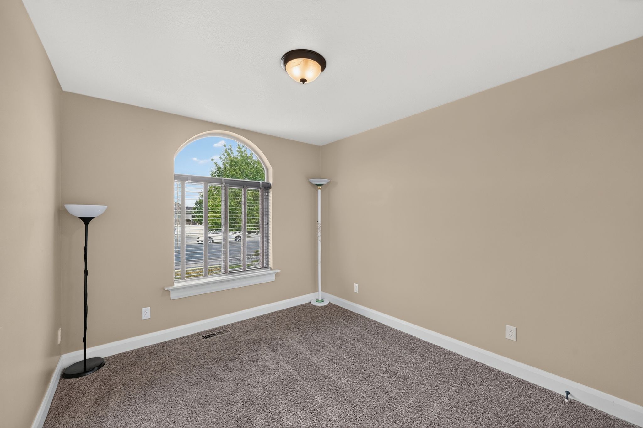 Room featuring an arched window with horizontal blinds, neutral wall paint, and textured carpeting
