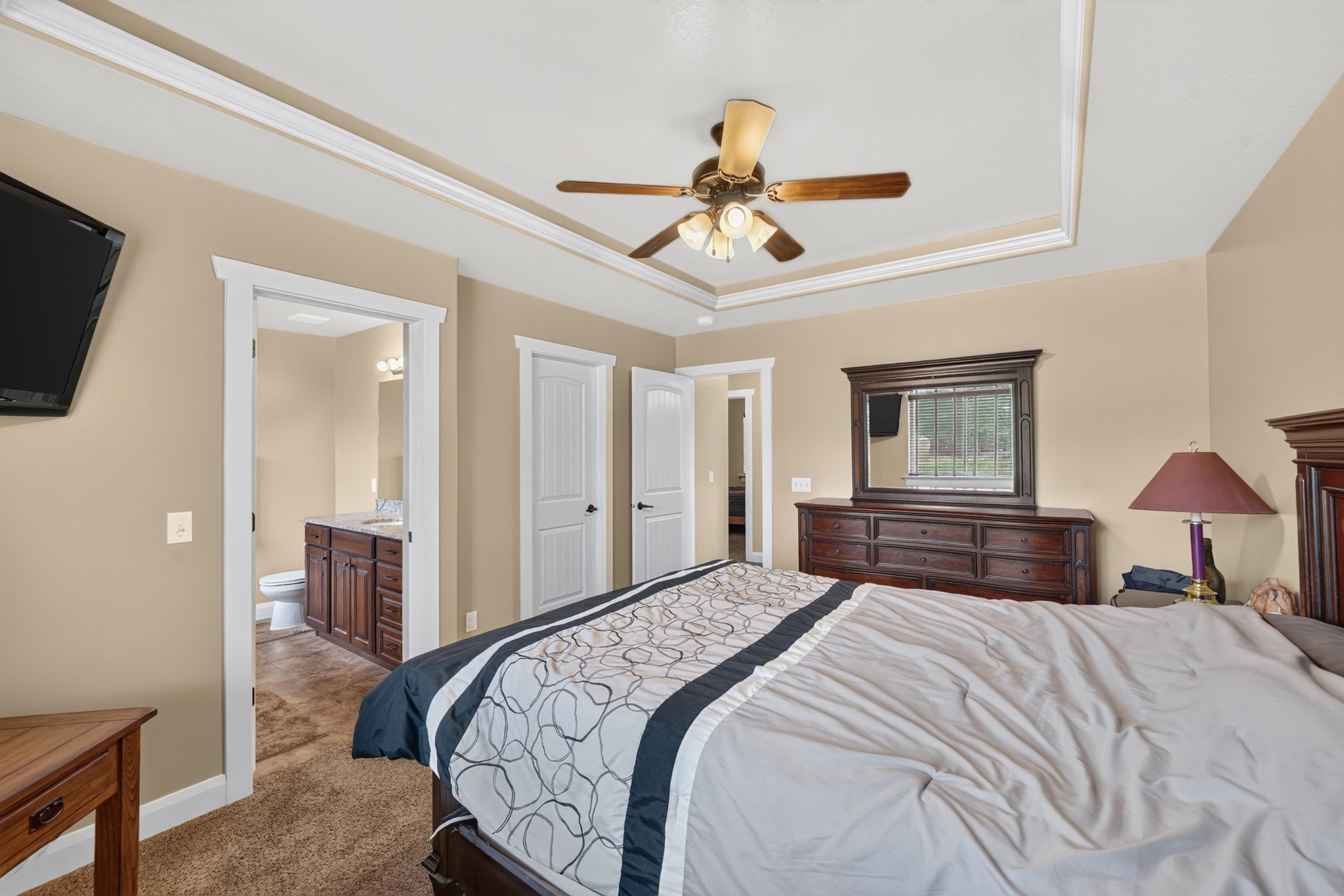Recessed tray ceiling with crown molding, ceiling fan, and warm-toned wall paint