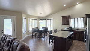 Kitchen with freestanding refrigerator, a center island, dark wood finish cabinetry, a breakfast bar area, and a high textured ceiling
