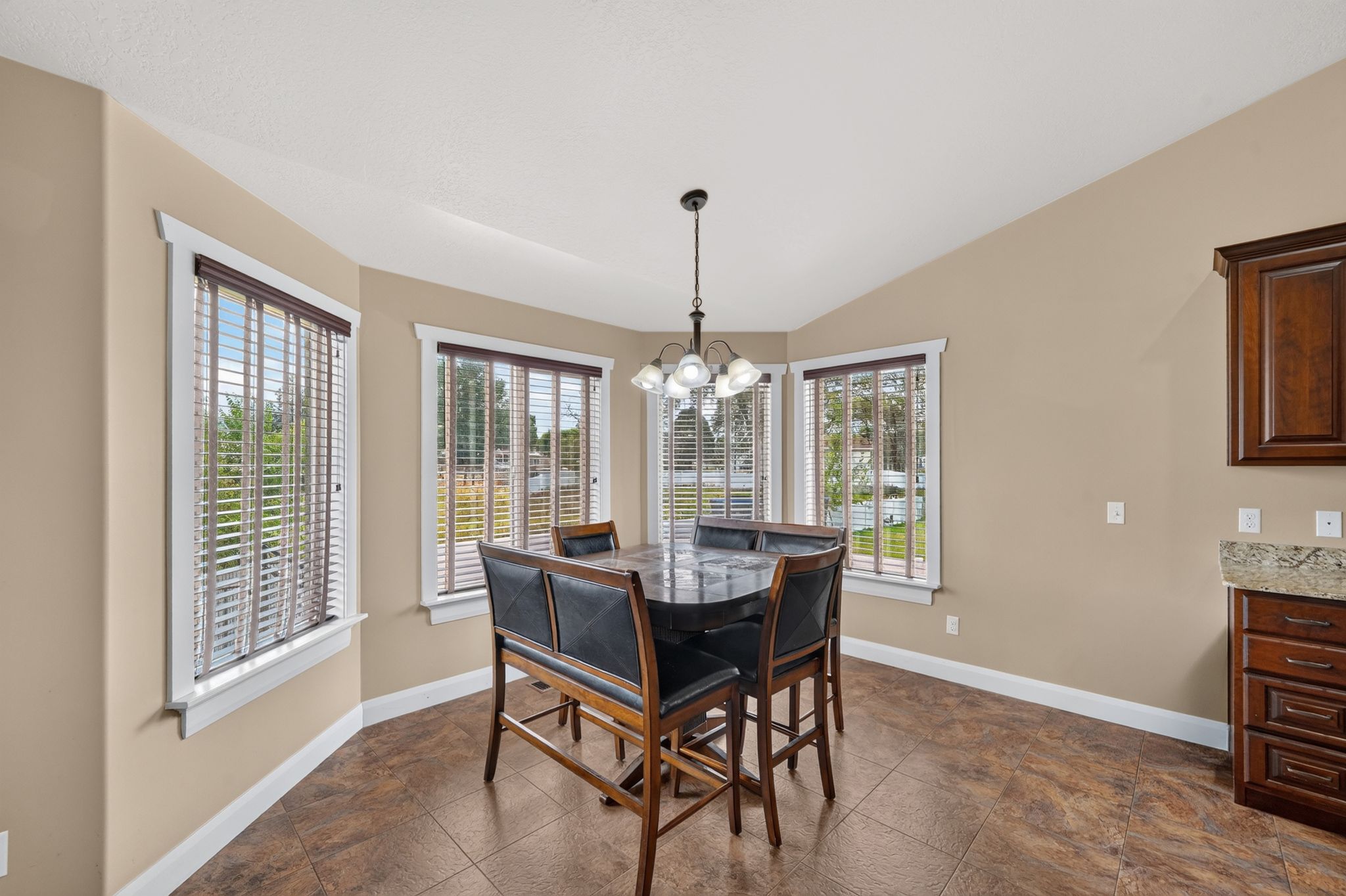 Breakfast nook featuring bay windows with blinds, a vaulted ceiling, a hanging chandelier, and tile flooring