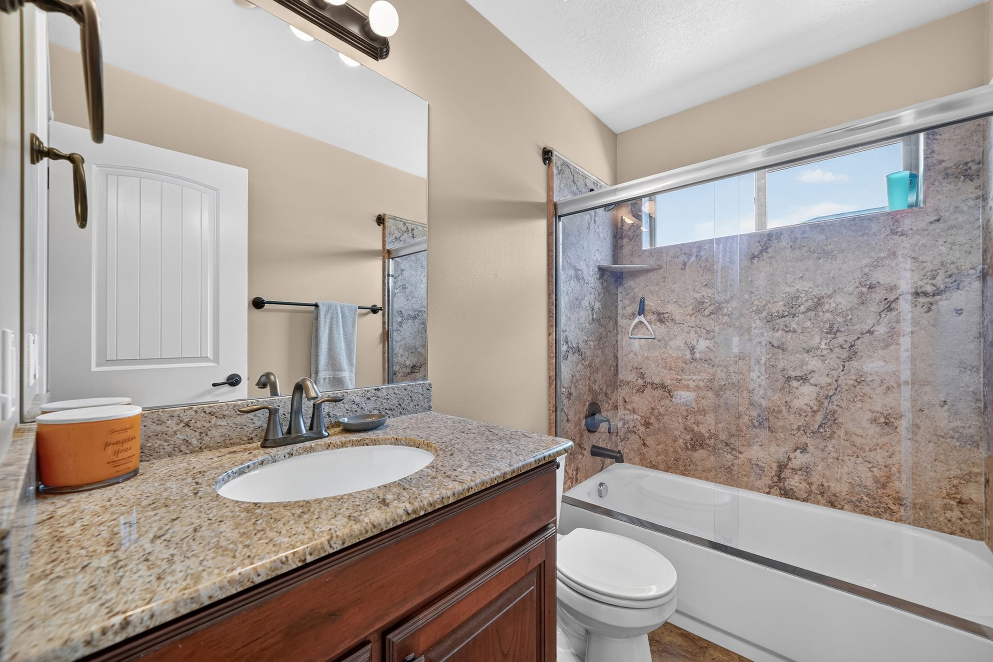 Bathroom featuring a granite countertop vanity with an undermount sink, a tub/shower combination with stone-look wall surrounds, and a transom window