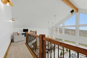 Hallway featuring light colored carpet, beamed ceiling, and hanging lights